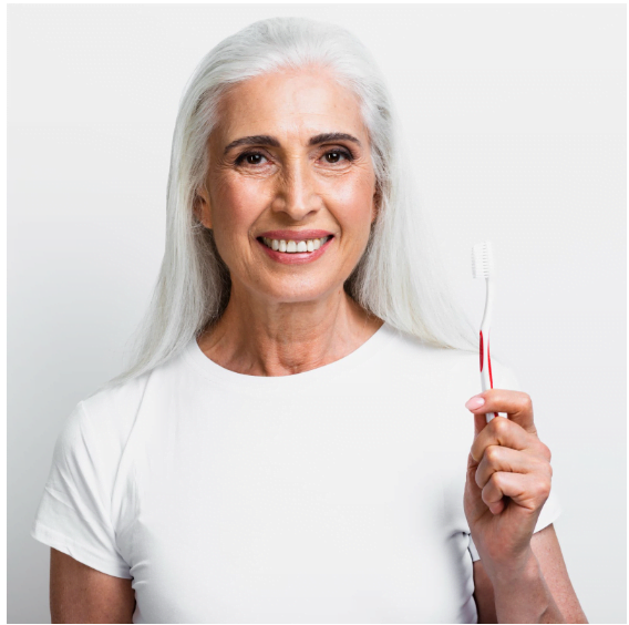 <alt="elderly woman smiling holding tooth brush">