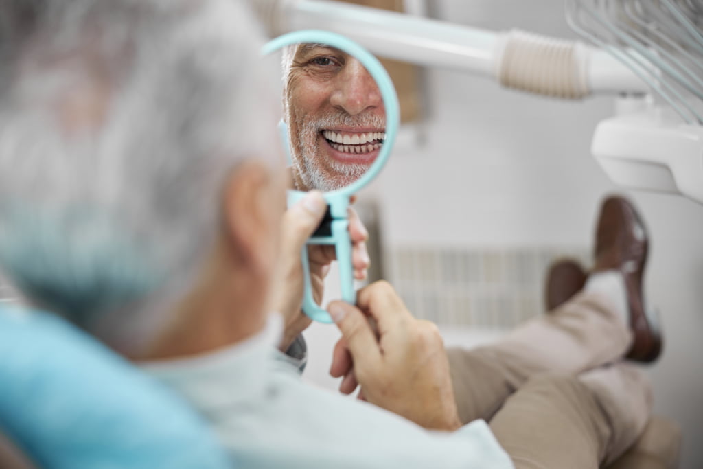 aged patient sitting in dental patient chair looking at himself in mirror