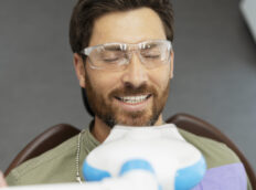man wearing glasses sitting in dental chair whilst dentist checks his teeth